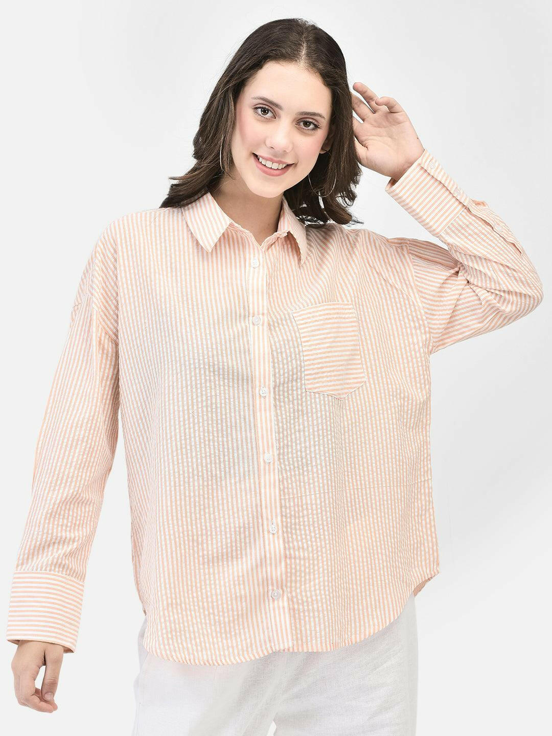 Model wearing peach striped button-up shirt with white pants. Image Description: "A smiling model showcases a casual yet stylish look, featuring a peach striped button-up shirt with long sleeves and a front pocket. She pairs the shirt with white pants, creating a fresh and comfortable outfit perfect for warm weather. The peach striped shirt is versatile and can be worn for various occasions, making it a great addition to any wardrobe. Ideal for those seeking a trendy and relaxed summer style.