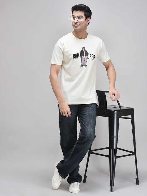 Beige graphic oversized t-shirt styled casually with dark denim – seated pose