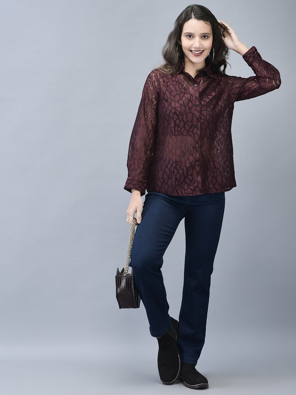 A woman standing, wearing a wine textured crochet shirt with full sleeves and a slim fit, paired with blue jeans and black boots.
