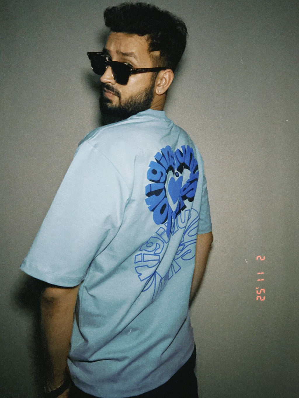 Person wearing a light blue t-shirt with a blue typography design on the back, standing against a plain background.